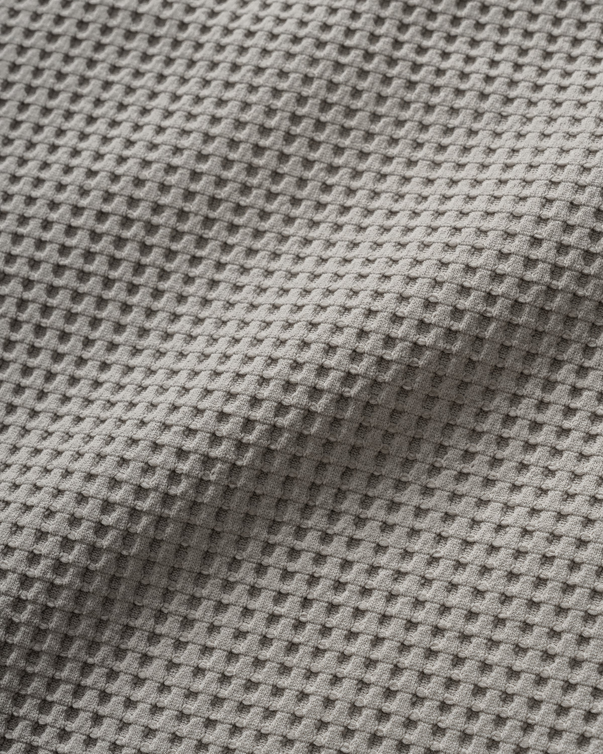 A close-up of a gray waffle-weave fabric texture with a raised grid pattern and soft folds.