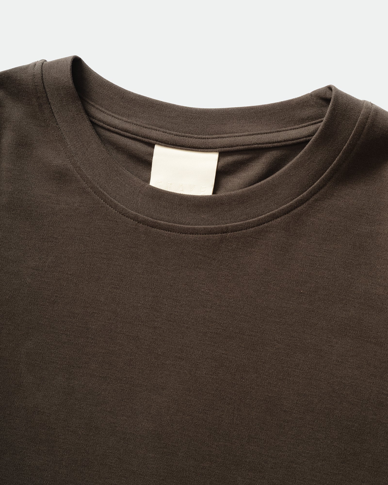 Close-up pack shot of GRAYE Cupro Signature Tee in Herbal Grey with a crewneck and branded label on a grey background.