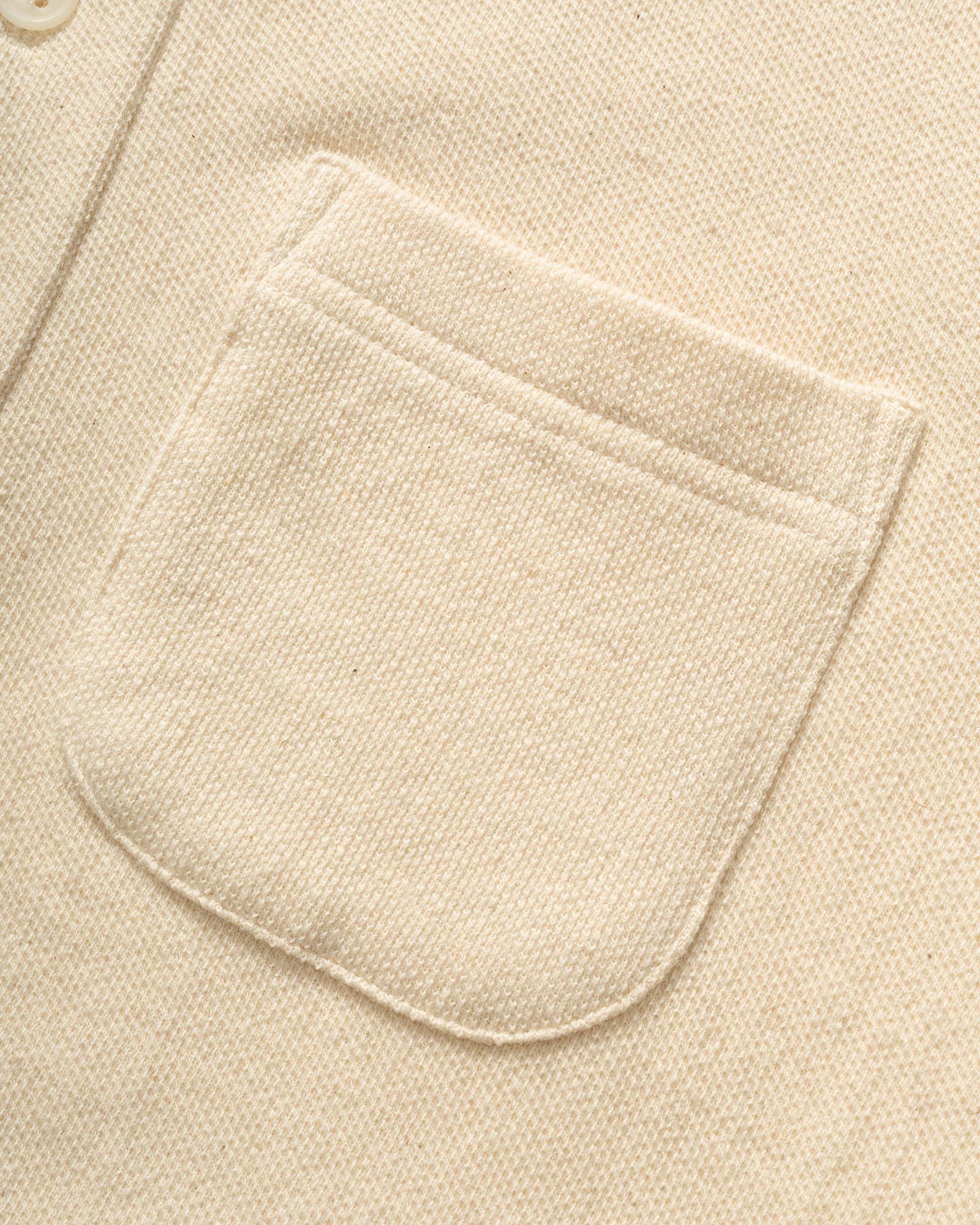 Close-up of IKIJI White Work Jacket patch pocket and textured fabric.