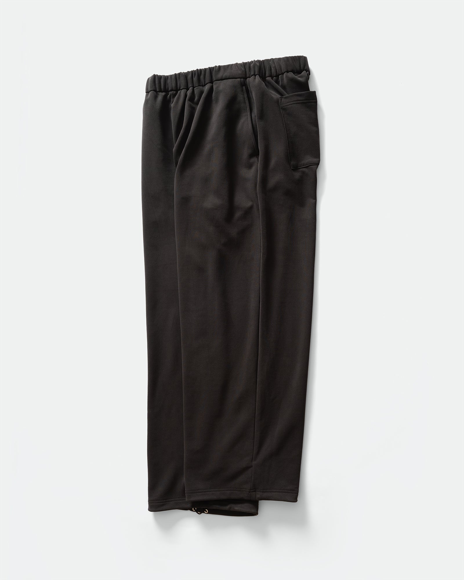 Side pack shot of KANAMASA PHIL Black Cupro Easy Pants with elasticated waistband and pocket on a grey background.