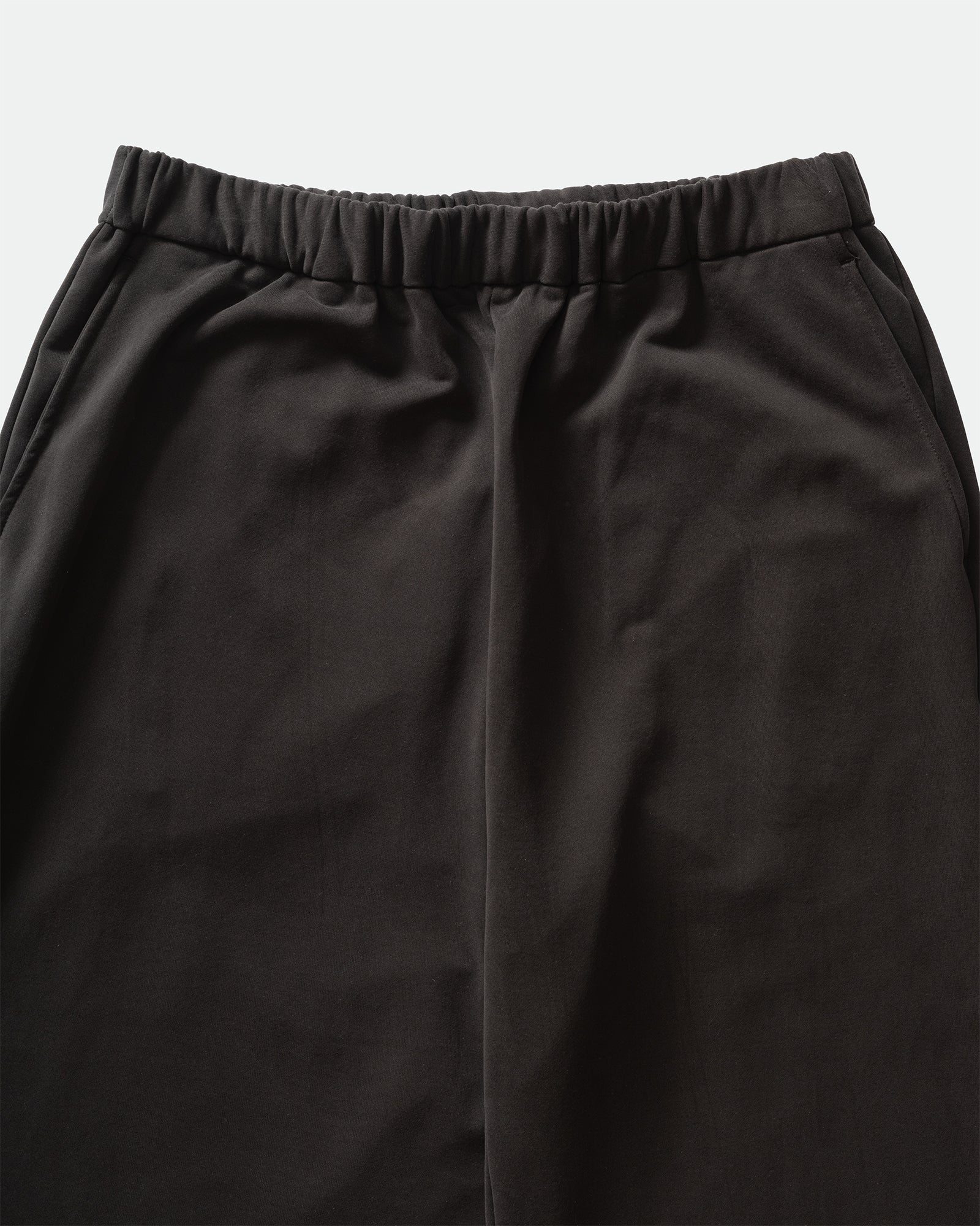 Close up of KANAMASA PHIL Black Cupro Easy Pants with elasticated waistband and slip pockets on a grey background.