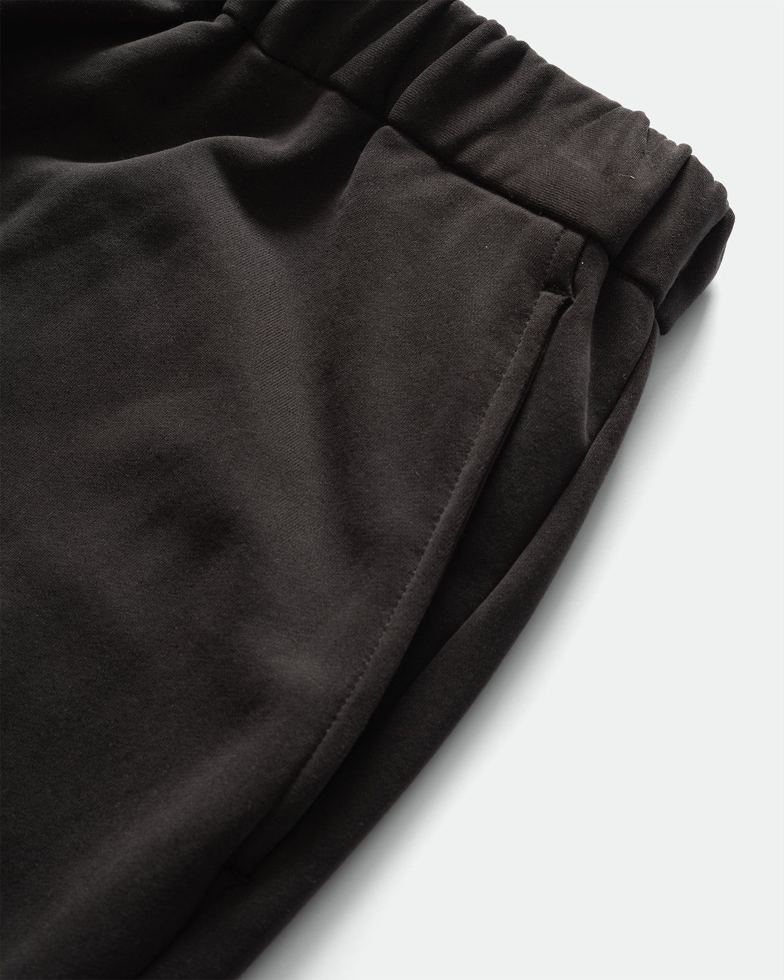 Close up of KANAMASA PHIL Black Cupro Easy Pants with elasticated waistband and slip pockets on a grey background.