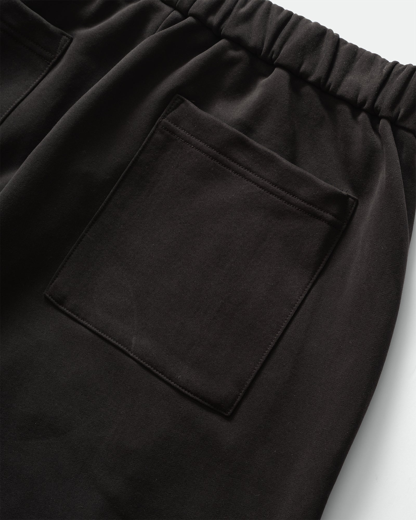Back close up of KANAMASA PHIL Black Cupro Easy Pants with elasticated waistband and patch pockets on a grey background.