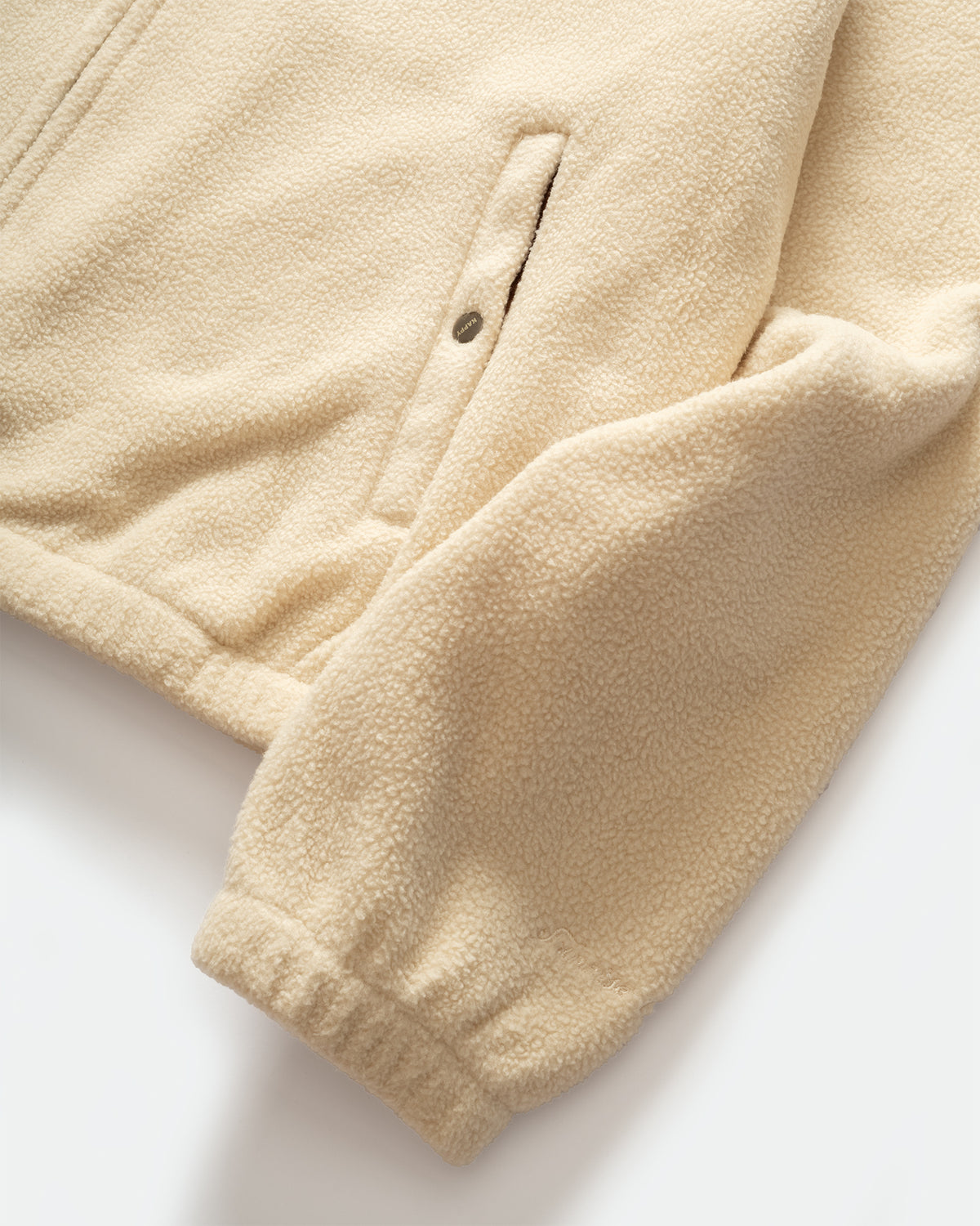 Close-up of Kappy beige fleece jacket sleeve with a ribbed cuff and a vertical zip pocket detail, shown on a clean white background.