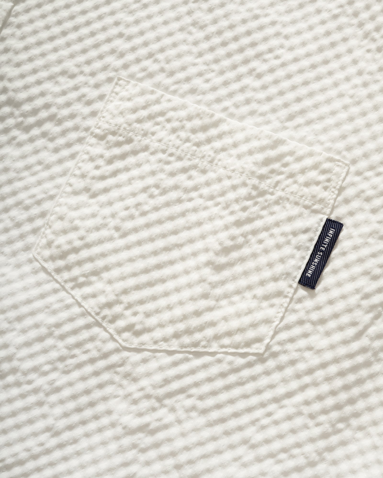 Close-up of Kappy White Seersucker Check Half Shirt, textured white fabric with branded label.