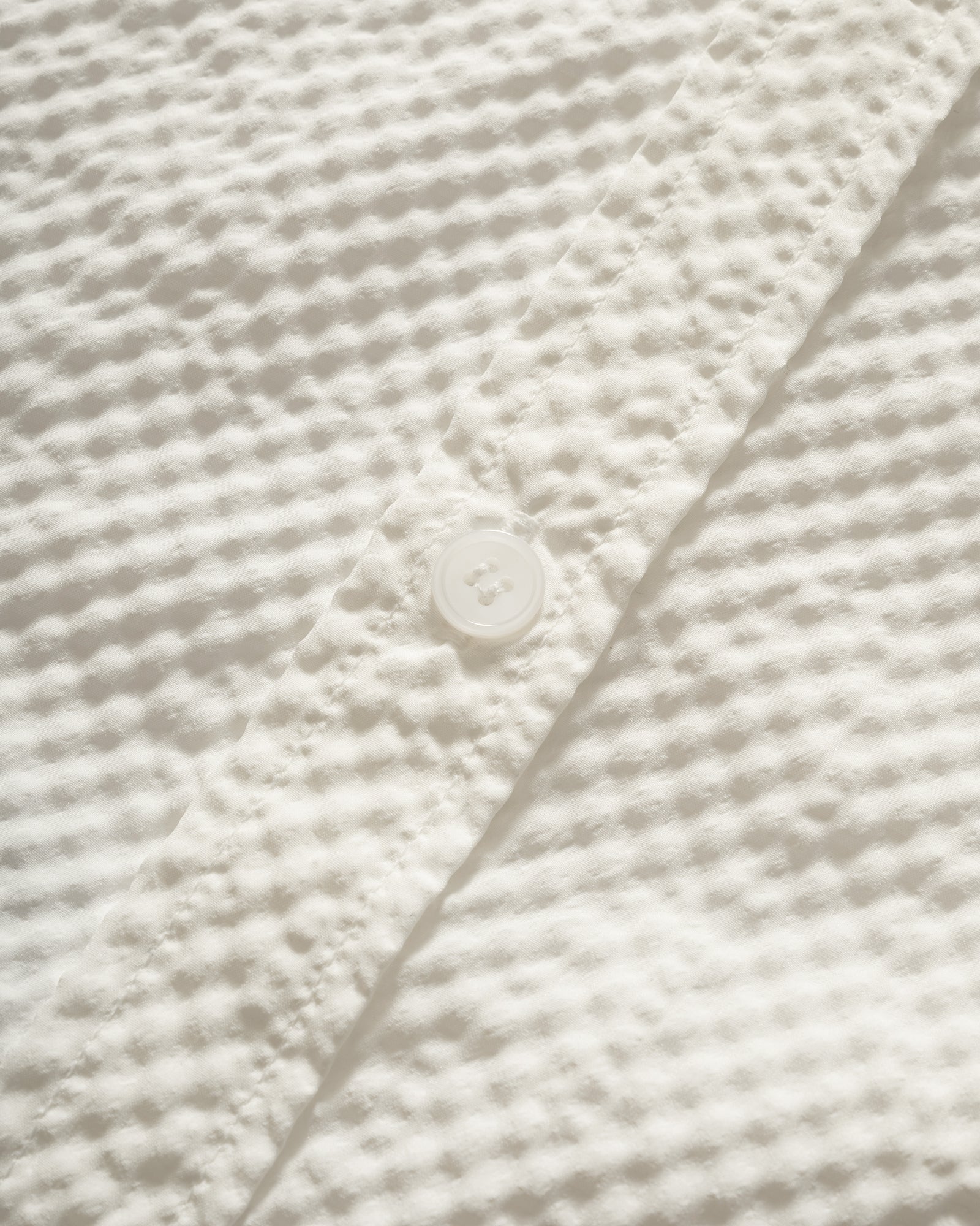 Close-up of Kappy Seersucker Check Half Shirt, textured white fabric with a button