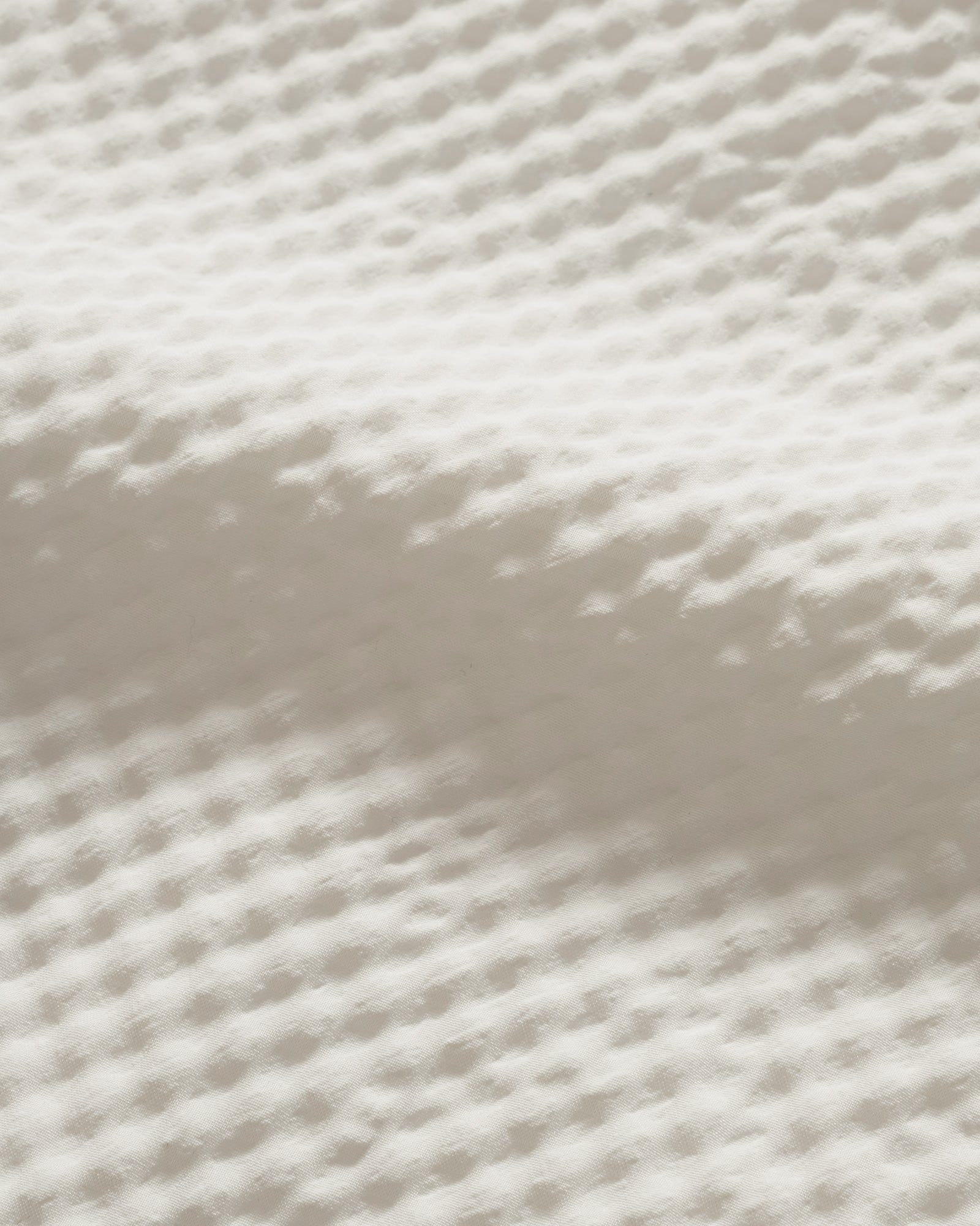 Close-up of textured white seersucker fabric with shadow. 