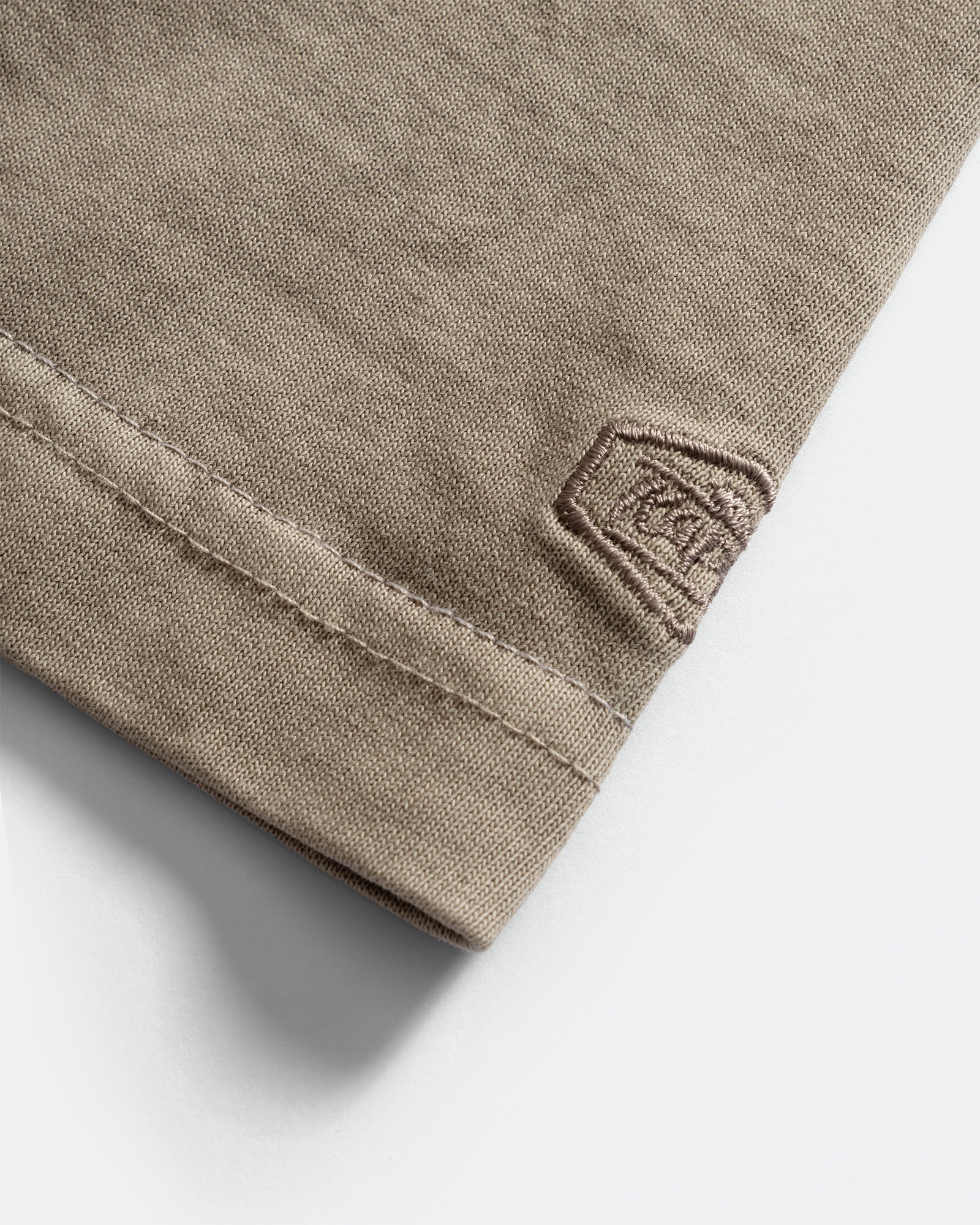 Close-up of a Kappy relaxed fit cotton mocha t-shirt sleeve with branded embroidery on a grey background 