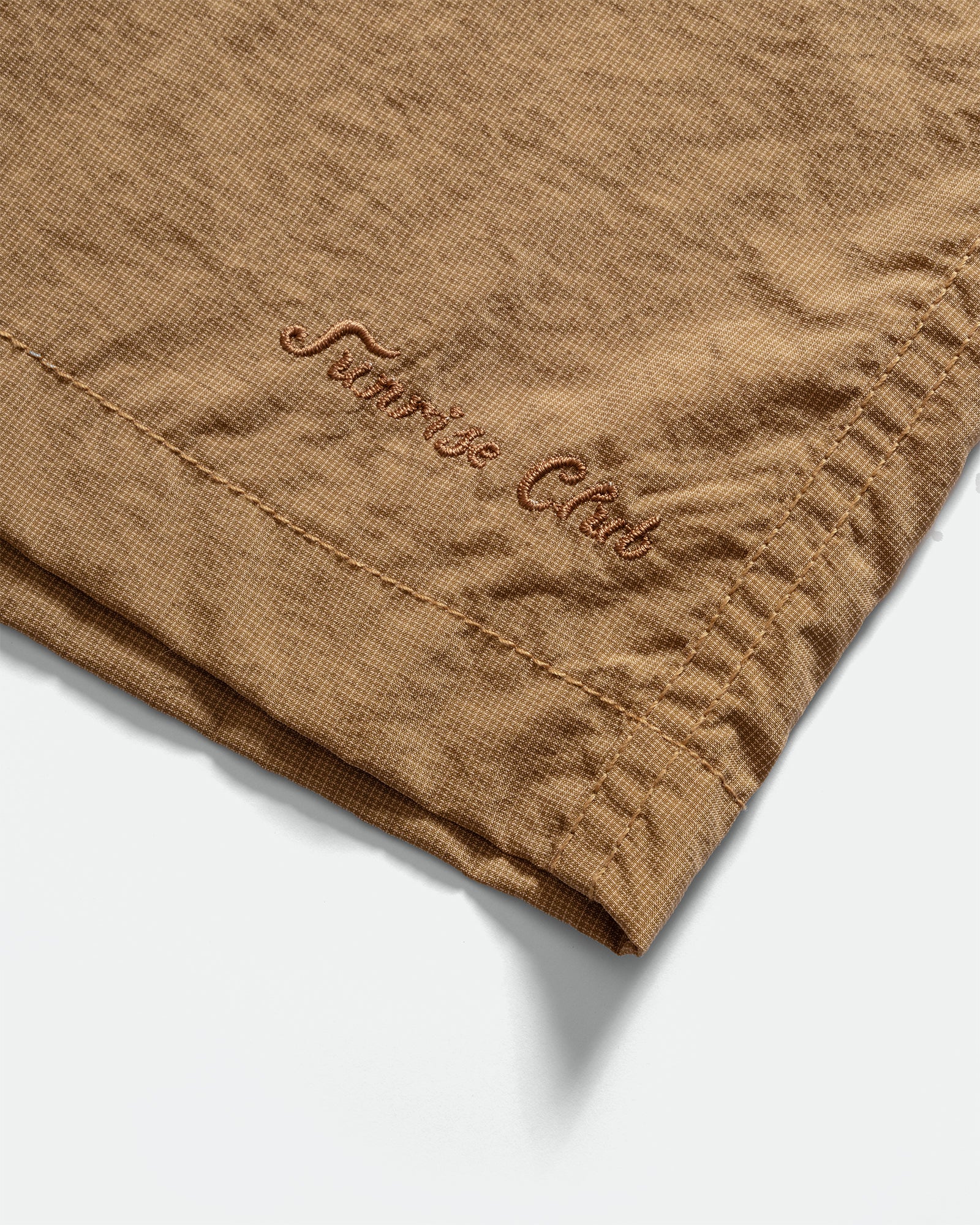 Close-up of a Kappy brown nylon shorts with 'Sunshine Club' embroidery on a grey background