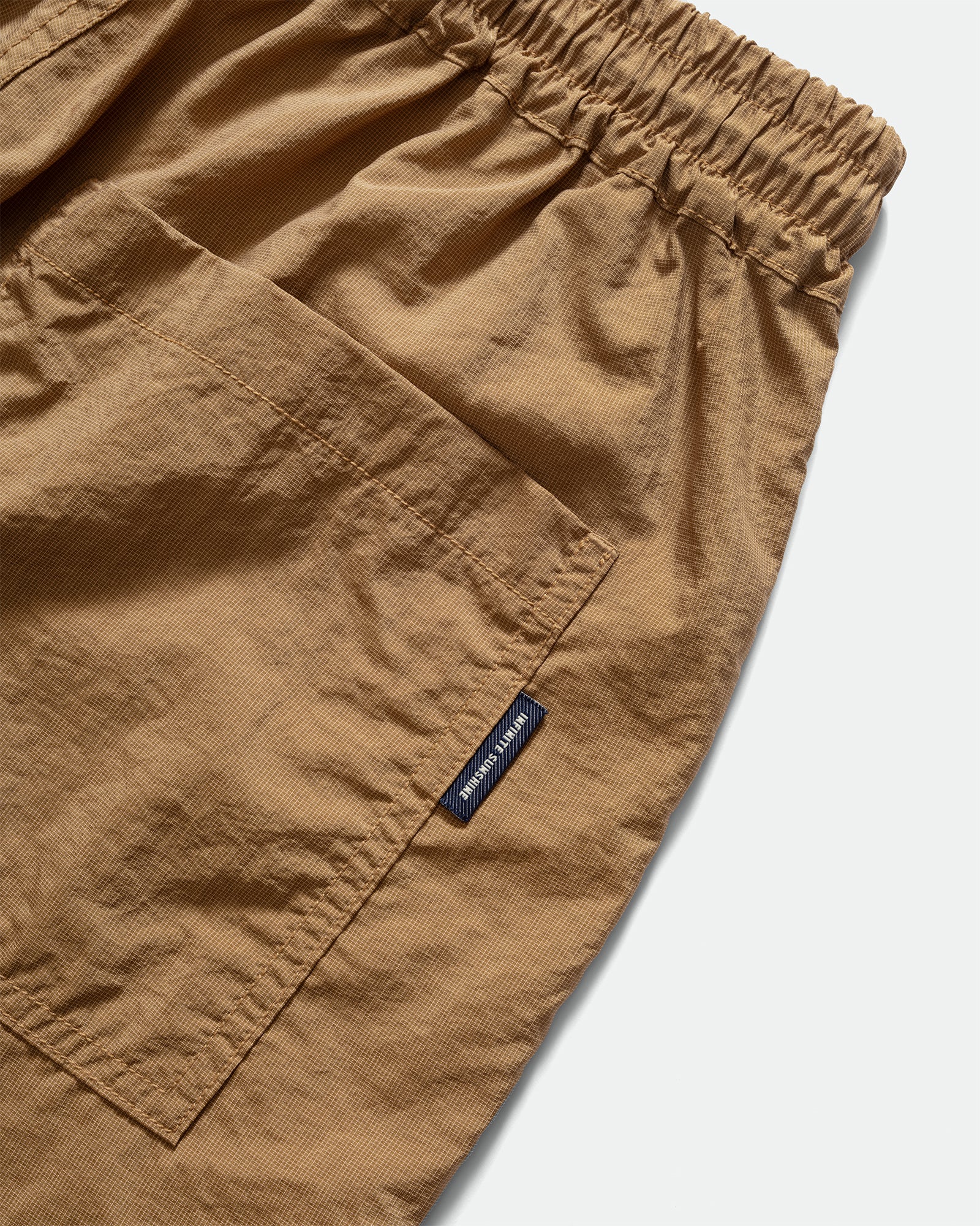 Close-up of Kappy brown nylon shorts with a brand label on back patch pocket a light gray background