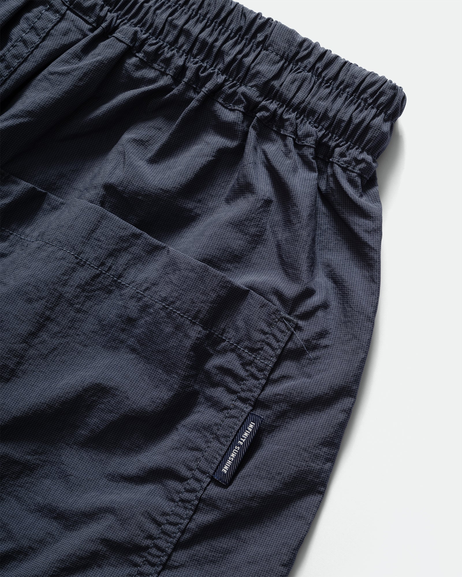 Close-up of Kappy brown nylon shorts with a brand label on back patch pocket a light gray background