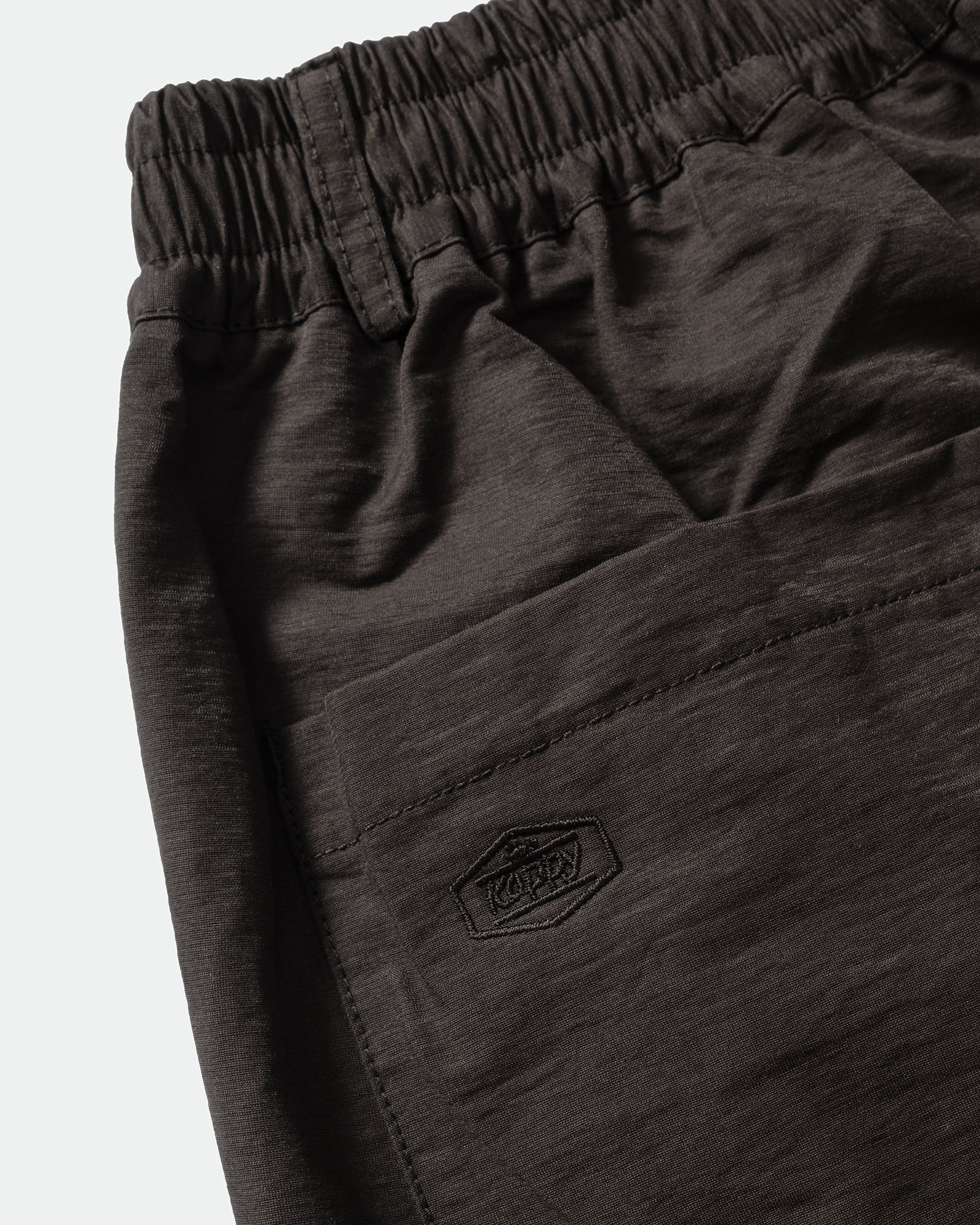 Close-up of black shorts with embroidered Kappy logo, elasticated waistband on a light grey background