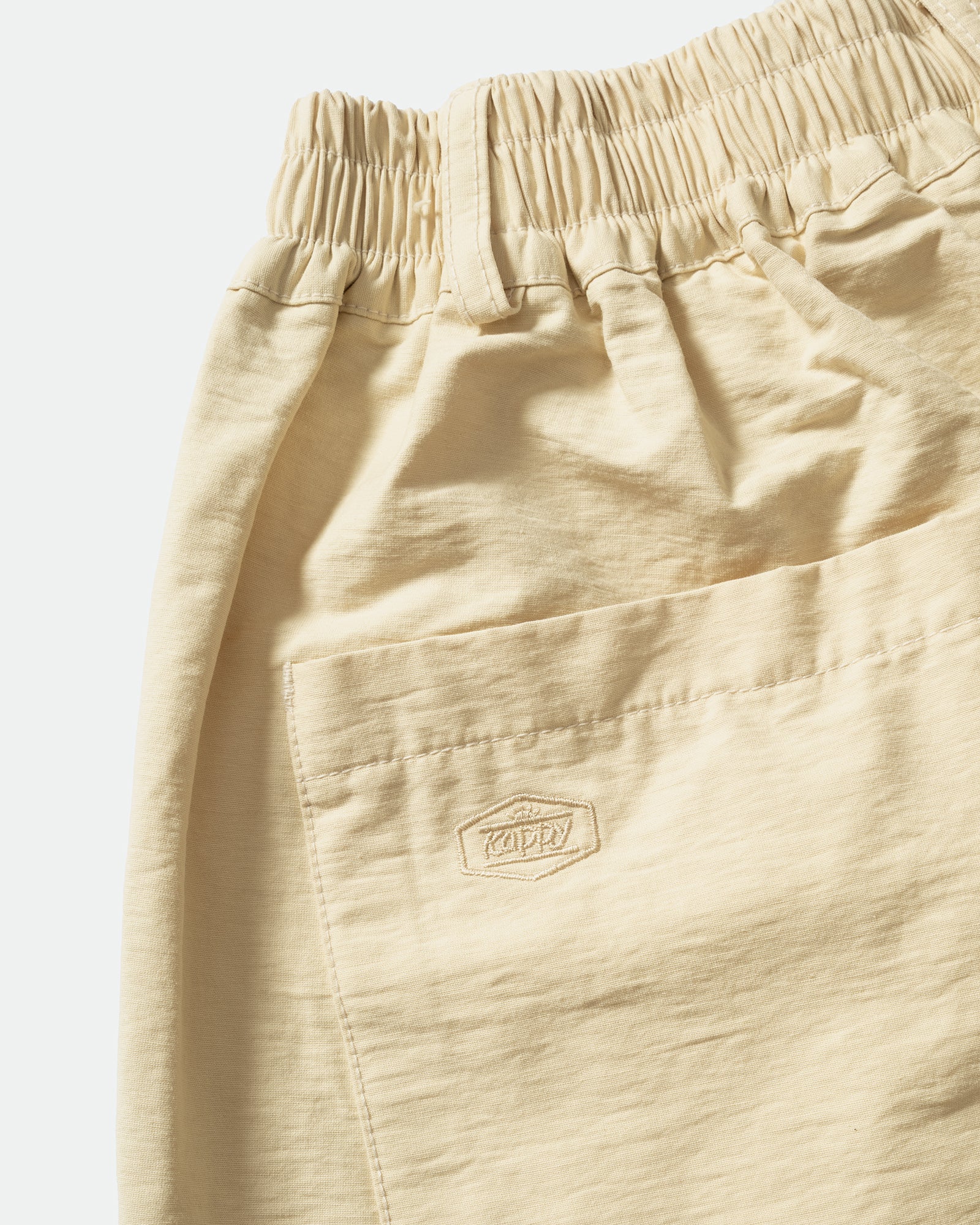 Close-up of black shorts with embroidered Kappy logo, elasticated waistband on a light grey background