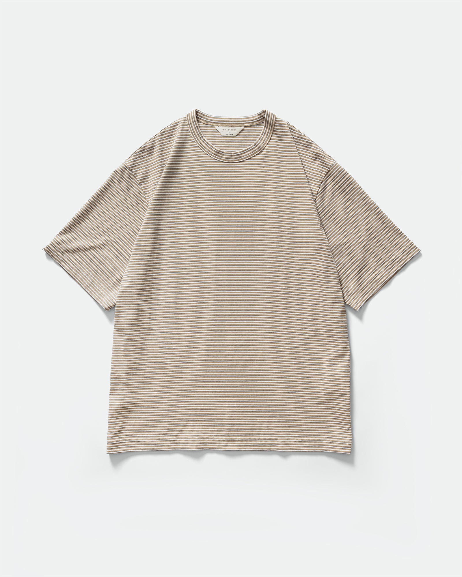 Packshot of Still By Hand Striped Beige White T-shirt with crewneck and short sleeves on a grey background
