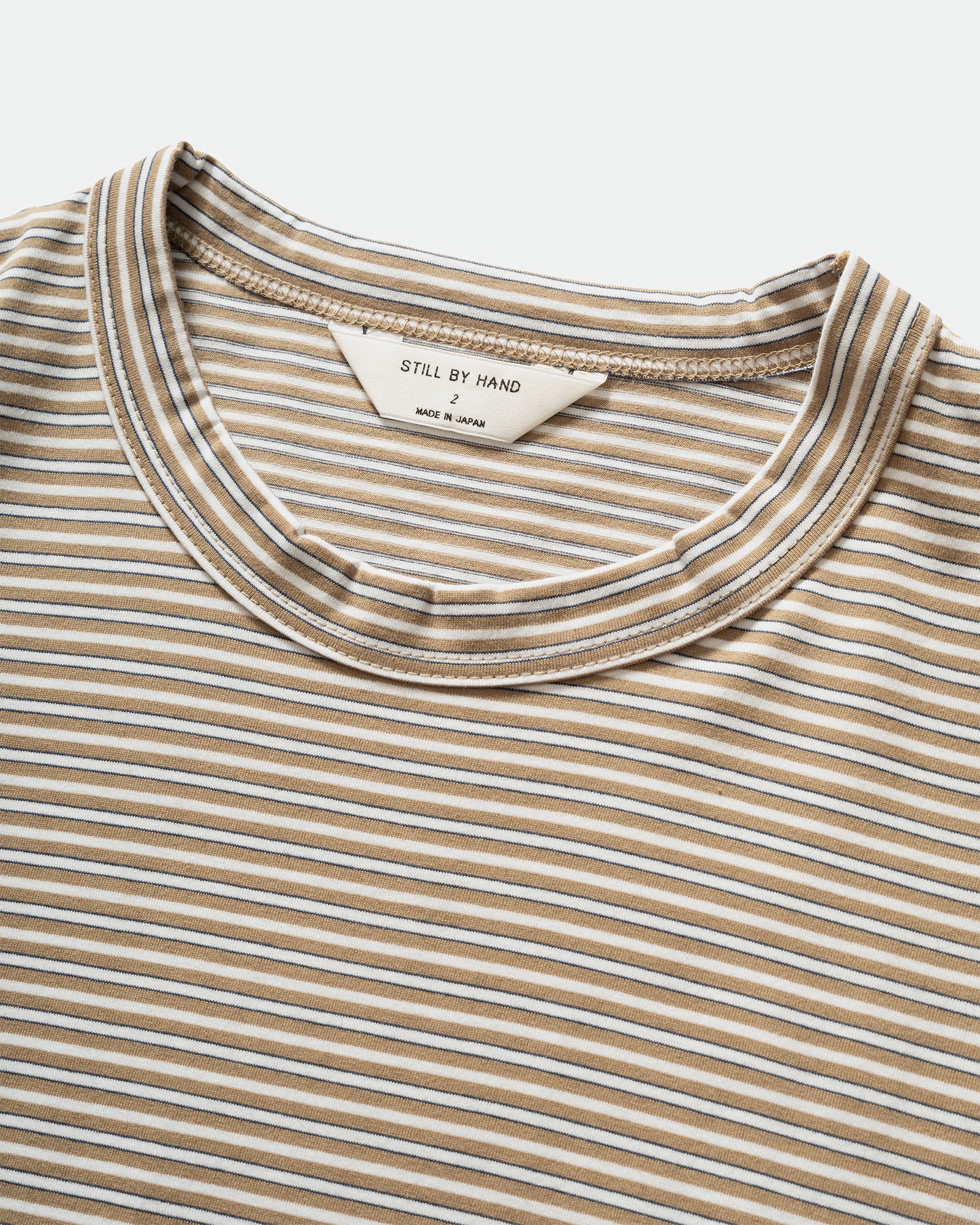 Pack shot of of Still By Hand Striped Beige White T-shirt crew neckline, label and stripe material on a grey background