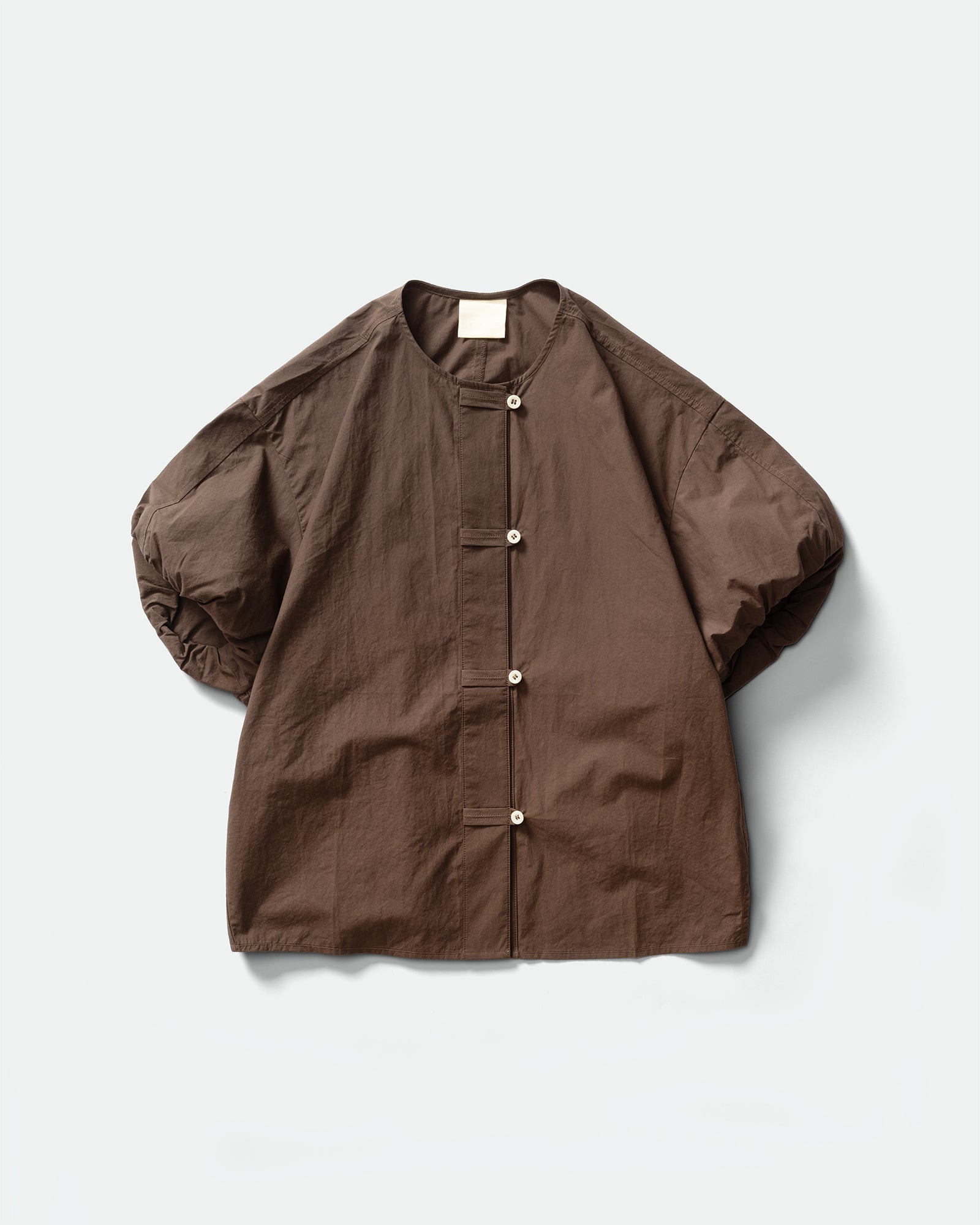 Pack shot of GRAYE Sun-Dried Cocoon Top in plum with an elasticated bubble sleeves, crewneck, and cord loop placket on a grey background.