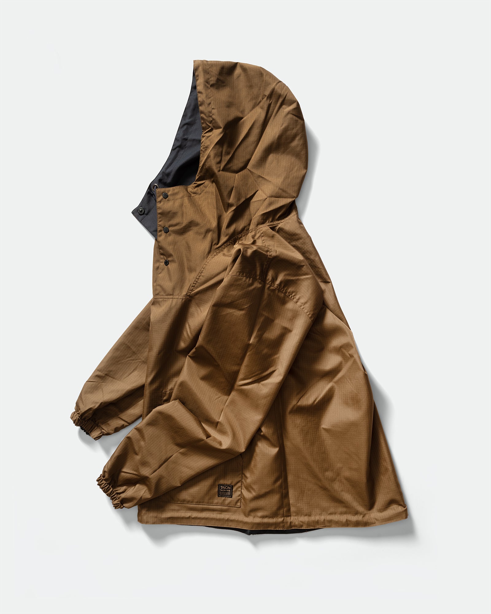 Side packshot of TAION Nylon Military Reversible Anorak Parka in Navy and Brown with snap button mock neck, drawstring hem, branded pocket on a grey background.