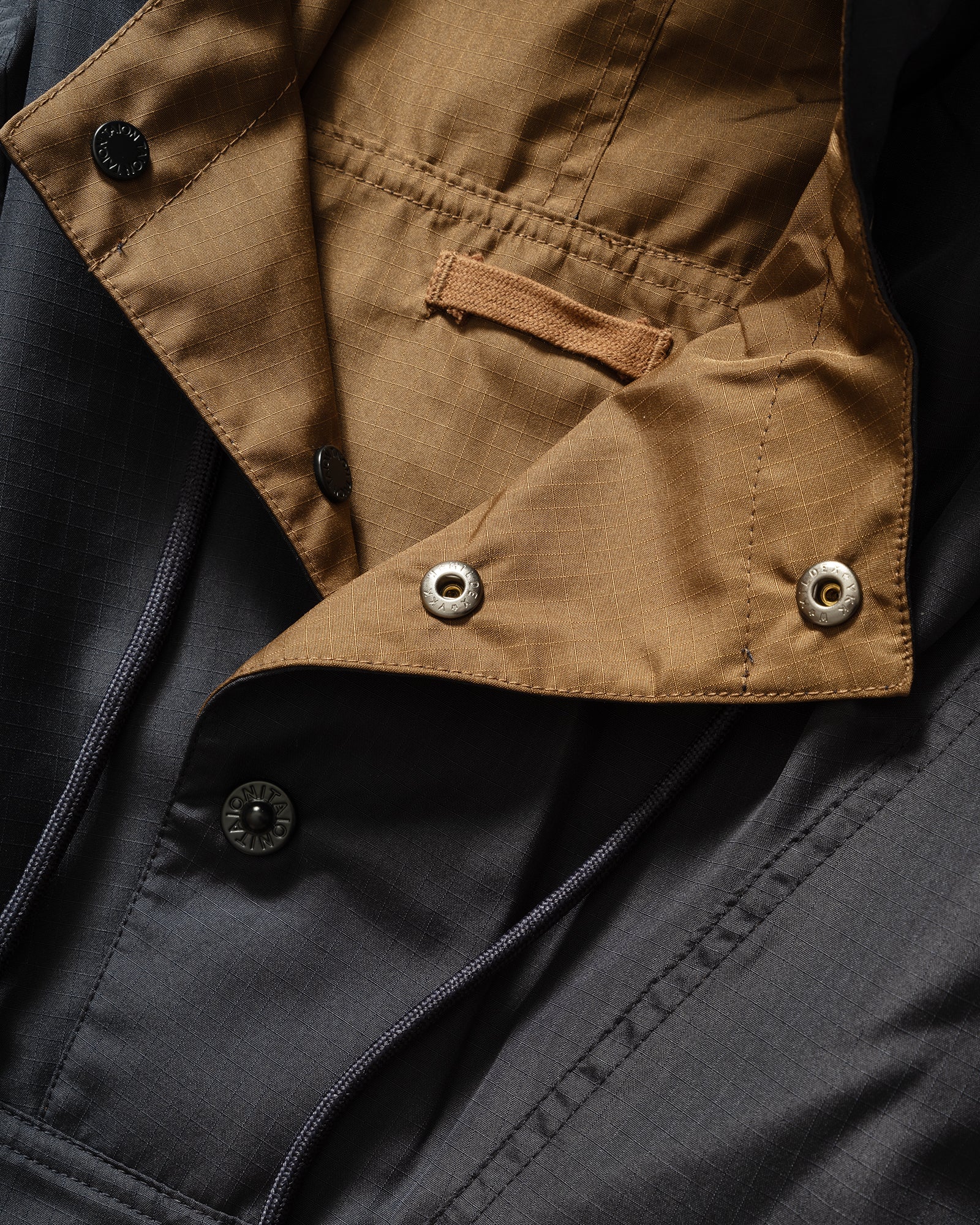 Close-up of TAION Nylon Military Reversible Anorak Parka in Navy and Brown with snap button mock neck, drawstring and hanger loop.