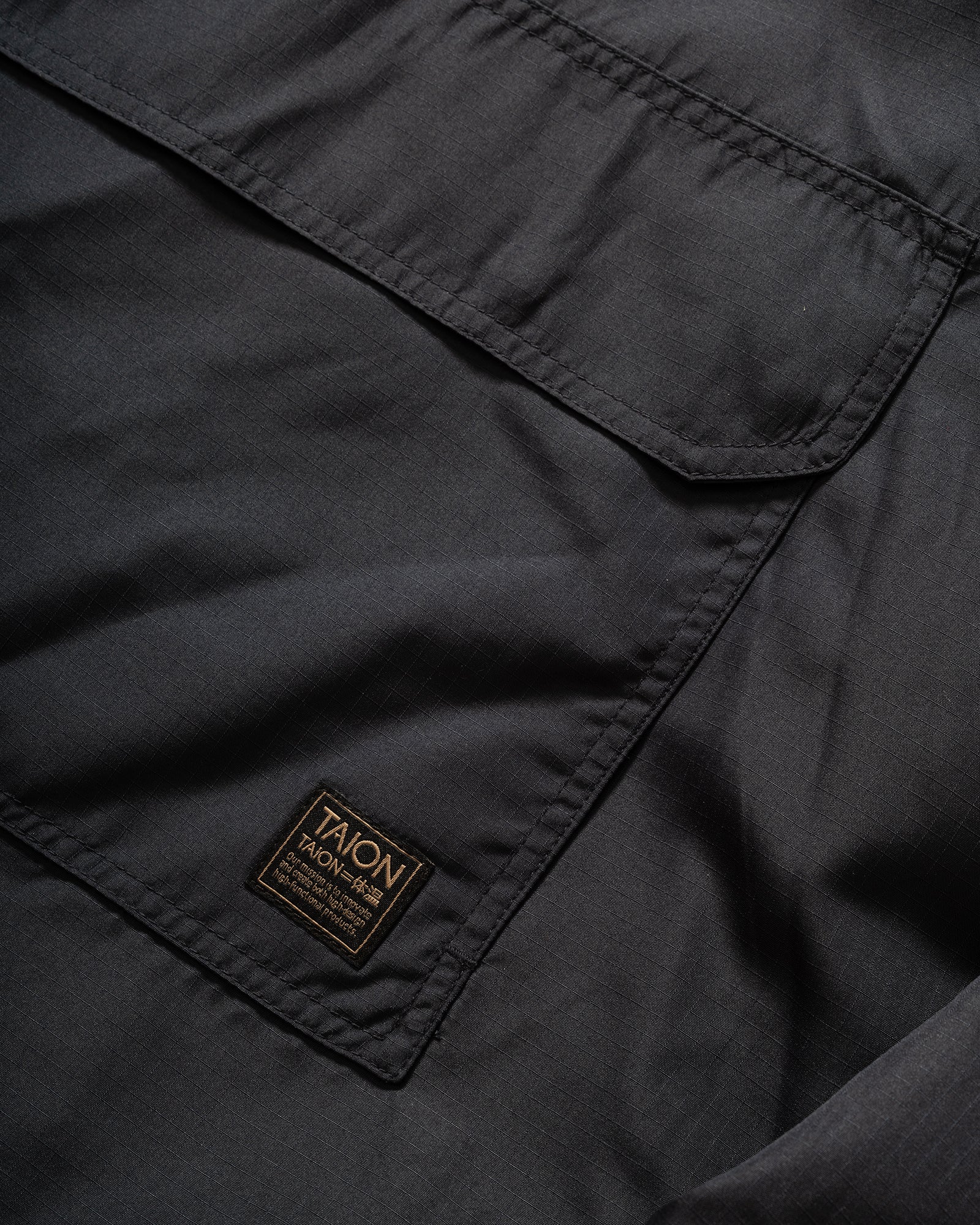 Close-up of TAION Nylon Military Reversible Anorak Parka in Navy and Brown with patch pocket and branded embroidery.