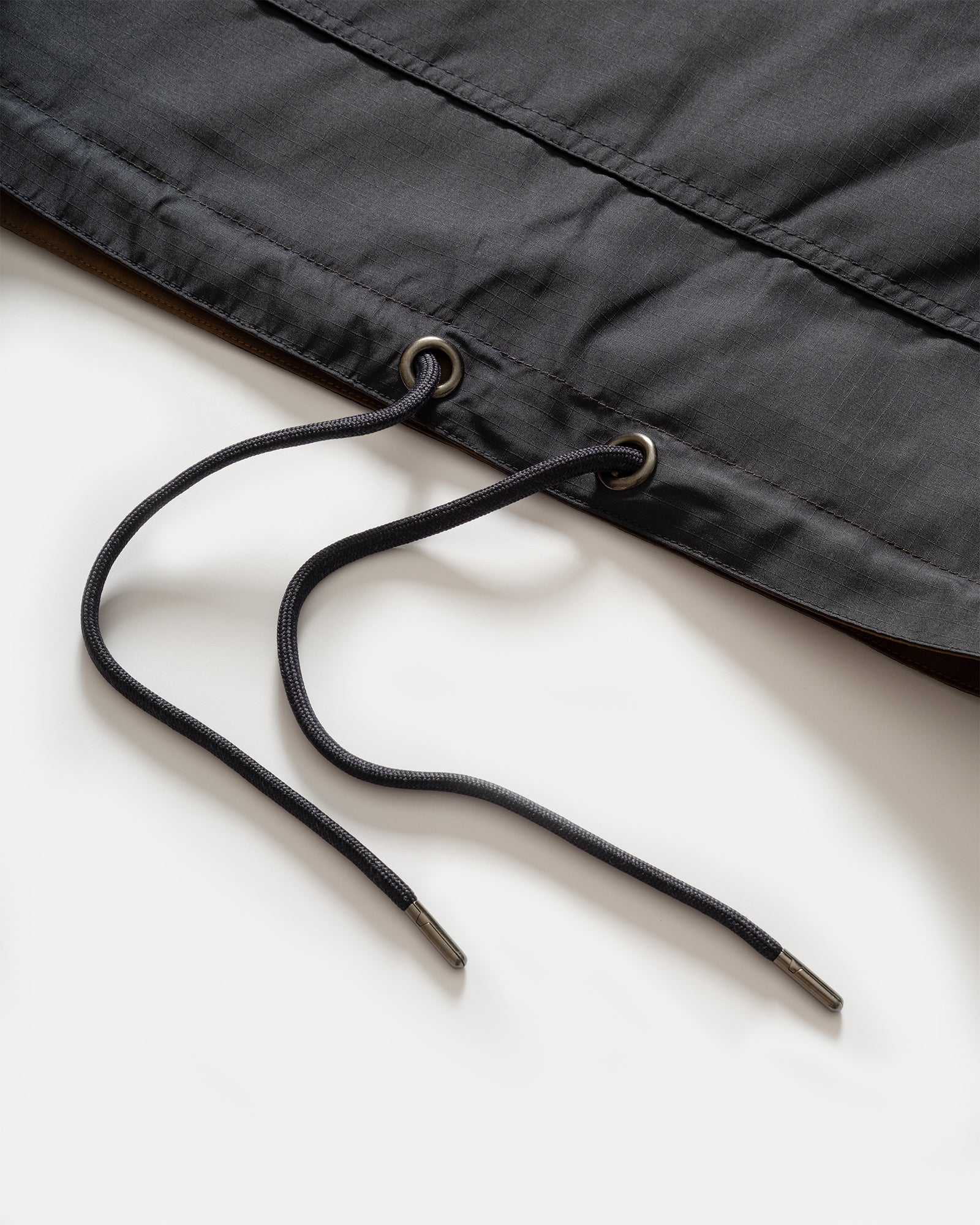 Close-up of TAION Nylon Military Reversible Anorak Parka in Navy and Brown with drawstring hem on grey background.