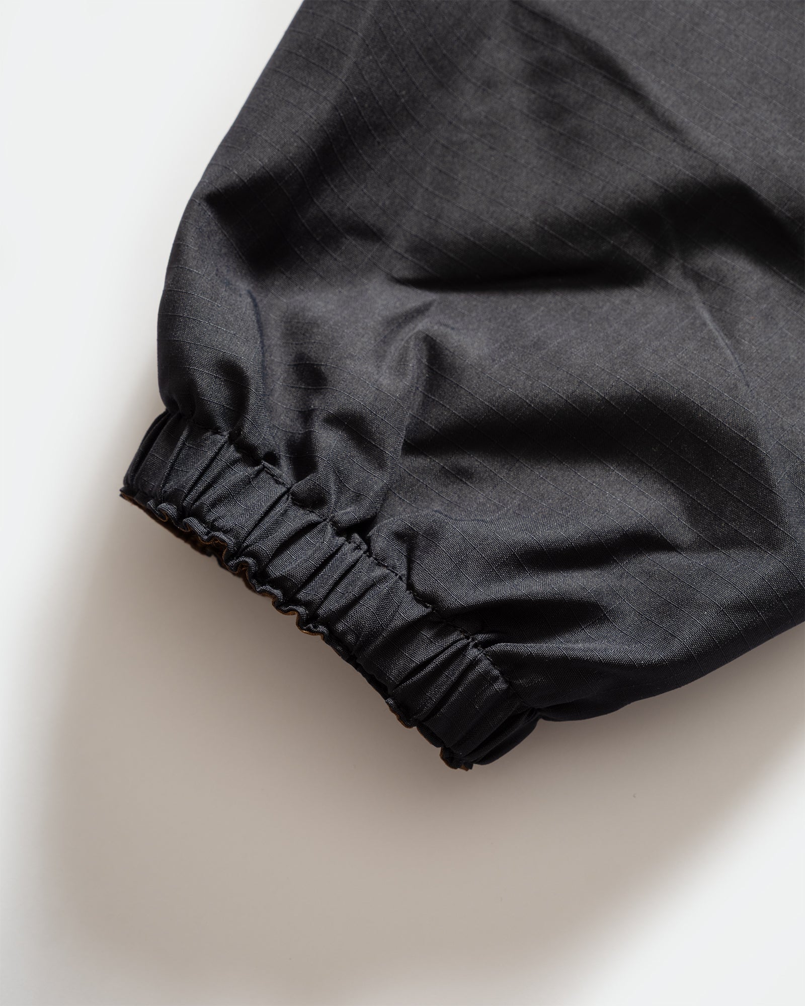 Close-up of TAION Nylon Military Reversible Anorak Parka in Navy and Brown with elasticated cuffs on grey background.
