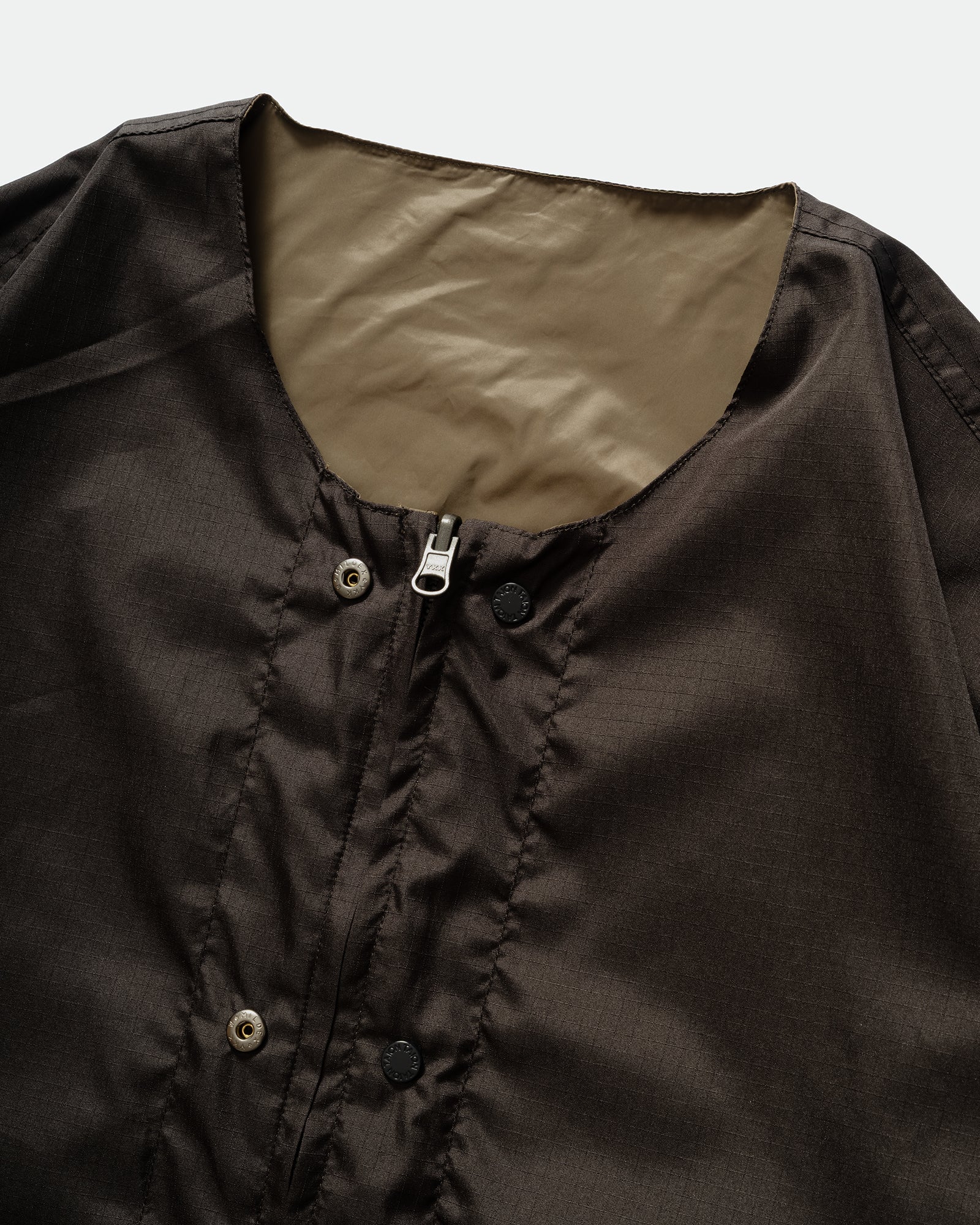 Close-up of TAION Nylon Military Reversible Liner Jacket in Dark Olive and Brown with zip closure, crewneck and metal branded buttons.